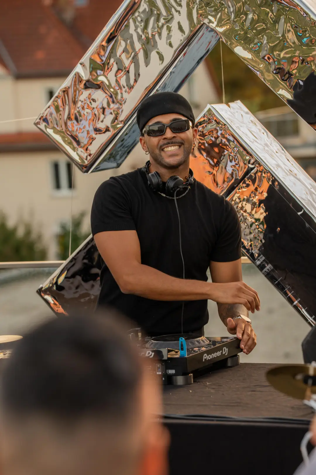 SEKOU laughing to camera at the decks, chrome sculpture behind him