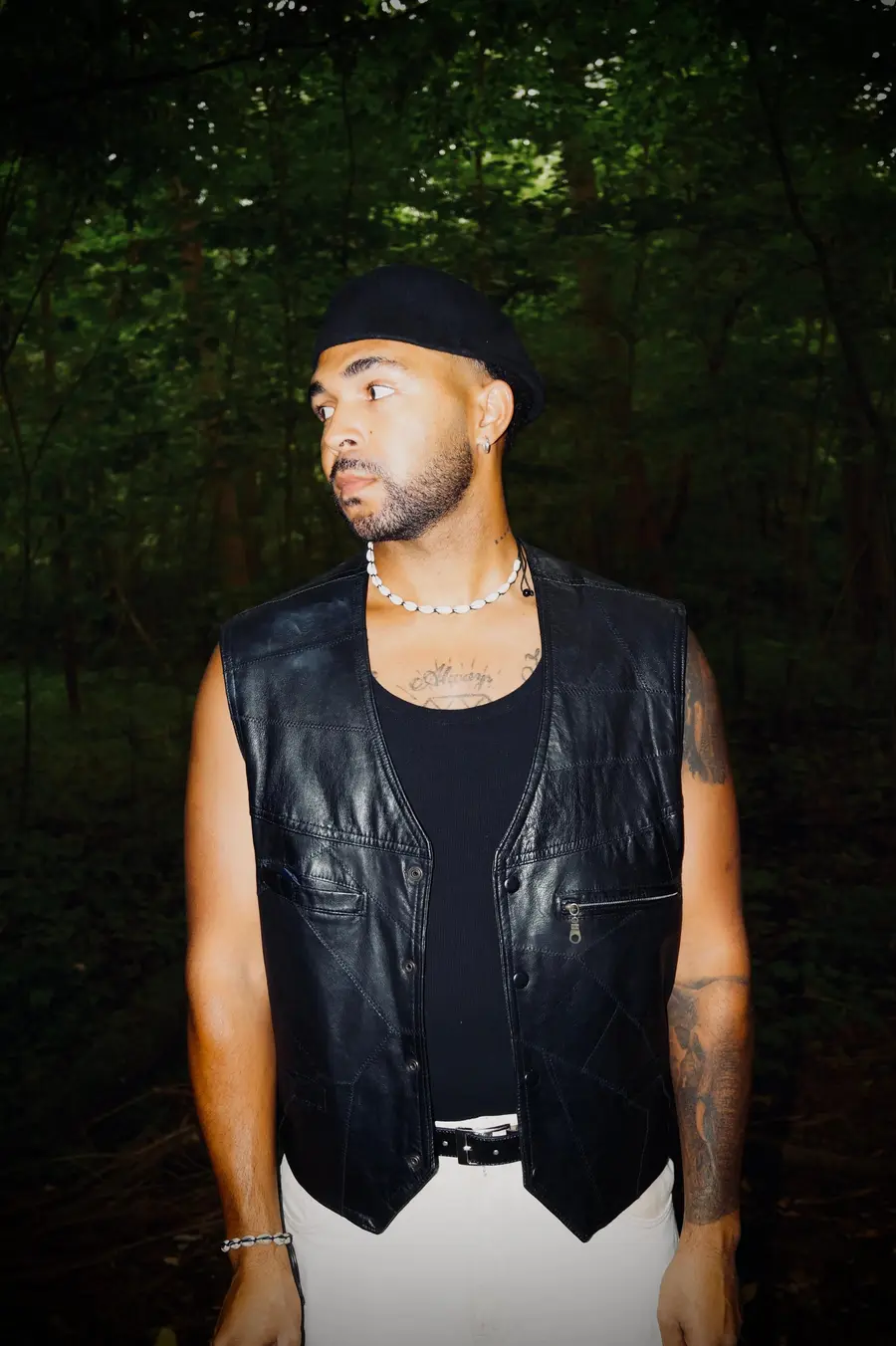 SEKOU in a leather vest and cap in a dark forest, looking aside